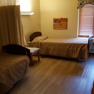 A simple and cozy room featuring two beds and minimal furniture, illuminated by natural light.