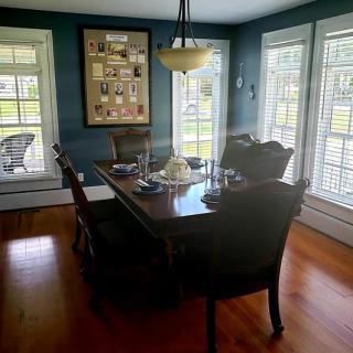 A well-lit dining room with a wooden table, chairs, and large windows.