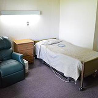 A simple hospital room featuring a bed, chair, and minimal medical equipment.