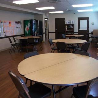 An empty cafeteria with round tables and chairs, featuring a vending machine in the corner.