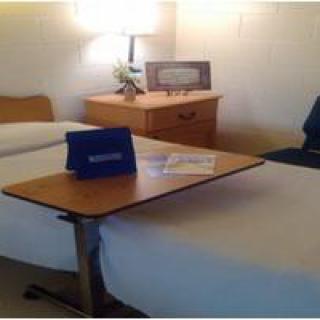 A hospital room with a bed, bedside table, and adjustable overbed table.
