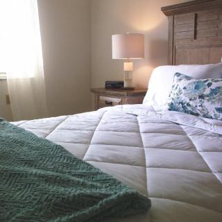 A cozy bedroom with a neatly made bed and a soft lamp on the bedside table.