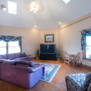 A spacious living room with a purple sofa, wooden flooring, and a large television.