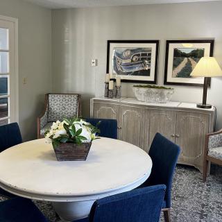 A cozy dining room with a round table, blue chairs, and decorative artwork on the wall.