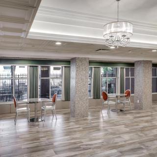 A spacious, modern lobby area with a chandelier, tables, and chairs near large windows.