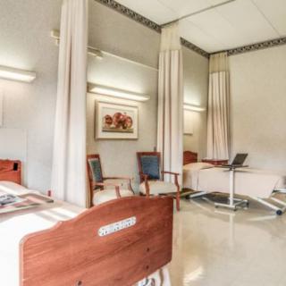 A well-lit hospital room with multiple beds and seating arrangements.