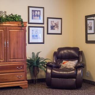 A cozy living room corner featuring a leather armchair, wooden cabinet, and decorative wall art.