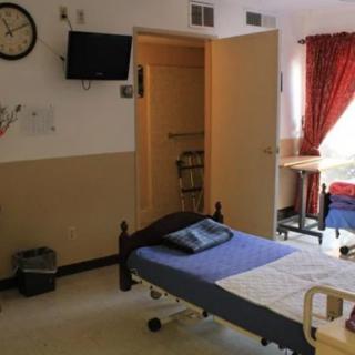 A hospital room featuring a bed, television, and medical equipment with curtains drawn near the window.