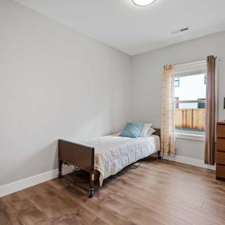A minimalist bedroom featuring a single bed with wooden flooring and a window dressed with curtains.