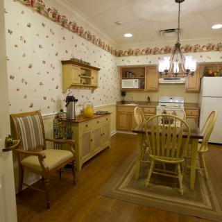 A cozy kitchen and dining area with vintage decor, featuring a wooden dining set, wallpapered walls, and a chandelier.