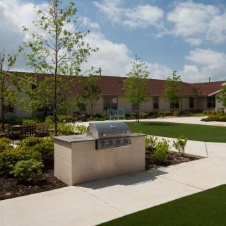 A well-maintained courtyard featuring a barbecue grill, surrounded by manicured landscaping and pathways.