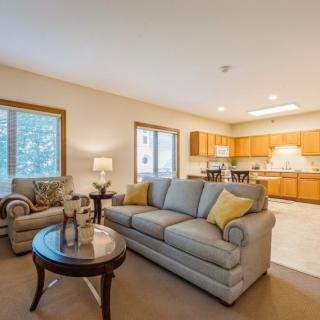 A cozy living room with an open floor plan leading to a kitchen, featuring comfortable seating and warm lighting.