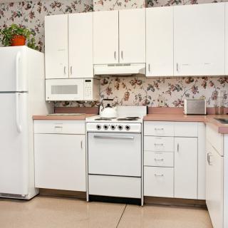A retro-style kitchen featuring white cabinets, a stove, refrigerator, and microwave with floral wallpaper.