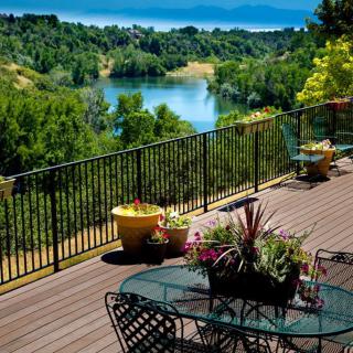A scenic terrace with outdoor seating overlooks a tranquil lake surrounded by lush greenery.
