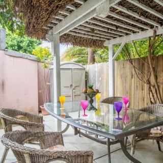 A cozy backyard patio with a pergola, wicker chairs, and a glass table adorned with colorful glasses.