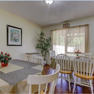 A cozy dining room with a table set, surrounded by chairs, highlighted by natural light through the window.