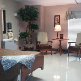A cozy room with chairs, a small table, a lamp, and a bed.