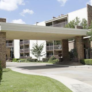 A modern building entrance with landscaped surroundings and a covered driveway.