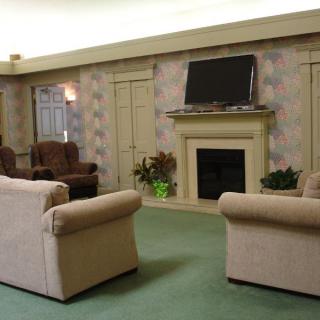 A cozy living room with beige sofas, armchairs, a fireplace, and a TV above it.