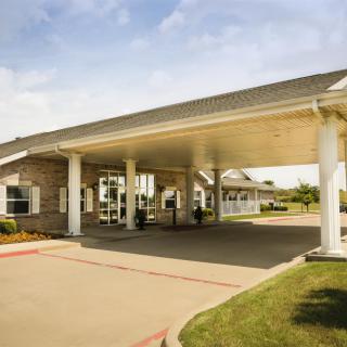 A building with a large covered entrance supported by columns, surrounded by landscaped areas.