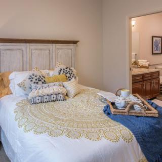 A cozy bedroom with a neatly made bed, decorative pillows, and a woven blanket, featuring a wooden tray with a tea set.