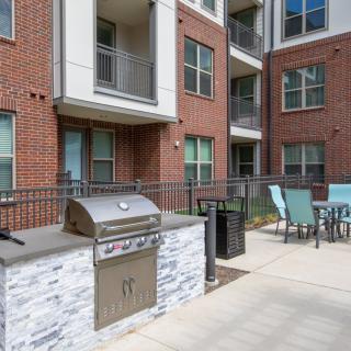 An outdoor patio area at an apartment complex, featuring a grill and seating.