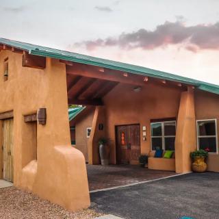 A southwestern adobe-style house with a green roof and modern features under a vibrant sunset sky.