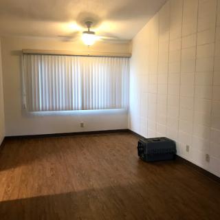 A spacious, empty room featuring a wooden floor and large window with blinds.