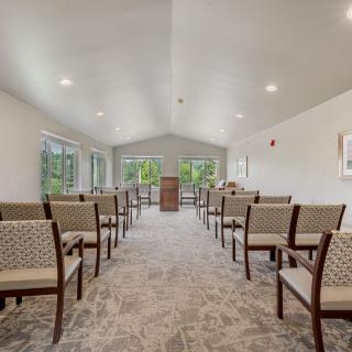 An interior view of a chapel with rows of chairs facing a podium and large windows.