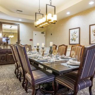 An elegantly designed dining room with a large table, set for a meal, surrounded by ornate chairs and illuminated by a chandelier.