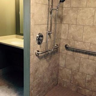 An accessible bathroom featuring a tiled shower with handrails and a vanity mirror.