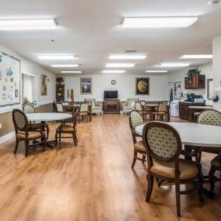 An empty dining room with multiple tables and chairs, featuring hardwood flooring and bright overhead lighting.
