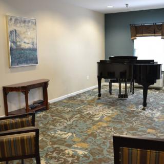 A cozy music room featuring a grand piano and seating, complemented by wall artwork.