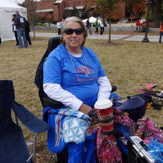 A person enjoying a festival outdoors in a wheelchair, wearing sunglasses and a t-shirt.