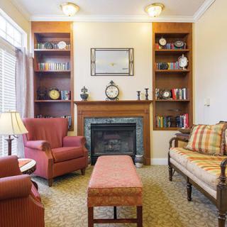 A cozy living room featuring a fireplace flanked by bookshelves, with armchairs and a sofa arranged around a central ottoman.