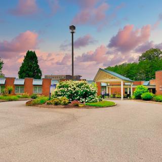 A serene view of a welcoming building surrounded by lush greenery and colorful flowers under a beautiful sky.