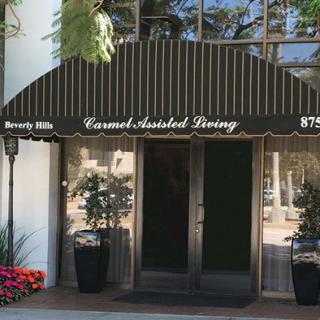 Entrance of Carmel Assisted Living with a striped awning and potted plants.