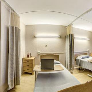 A well-lit hospital patient room featuring two beds, storage furniture, and curtains for privacy.