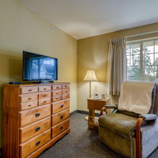 A cozy living room with a television on a wooden dresser, a comfortable chair, and a lamp by the window.