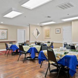 An indoor dining or meeting area with neatly arranged tables and chairs, covered with blue and patterned tablecloths.