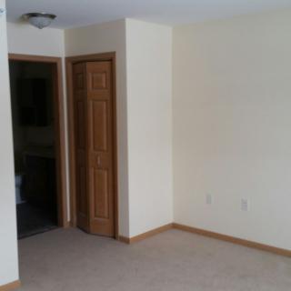 An empty room with beige walls, a wooden door, and a light fixture on the ceiling.