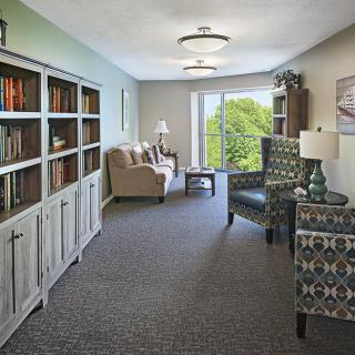 A cozy living room with bookshelves, seating area, and a large window offering natural light.