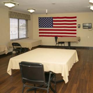 A meeting room with an American flag displayed on the wall, featuring tables and chairs arranged in the center of the room.