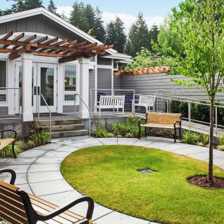 A charming garden space featuring a modern house with a pergola, surrounded by lush greenery and benches.