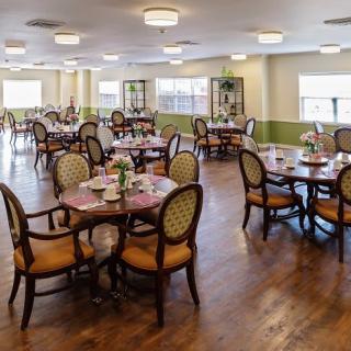 A spacious dining room with elegantly set tables and chairs, featuring a wooden floor and soft lighting.