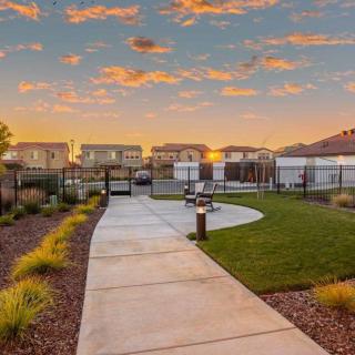 A suburban park at sunset with a sidewalk, benches, and houses in the background.