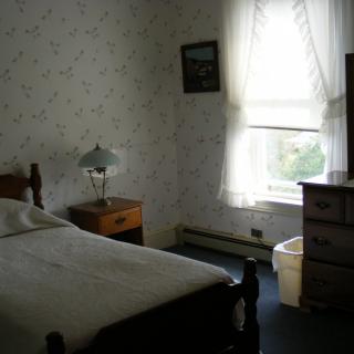 A cozy vintage bedroom with a single bed, nightstand, lamp, and dresser.