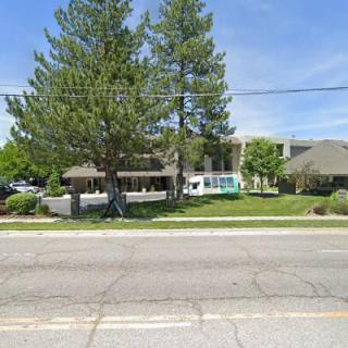 A building surrounded by trees with a road and sidewalk in the foreground.