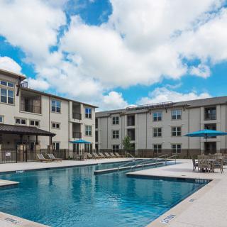 A modern apartment complex with a large outdoor swimming pool under a partly cloudy sky.