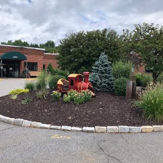 A colorful garden featuring a decorative train, surrounded by various plants and flowers at the entrance of a building.